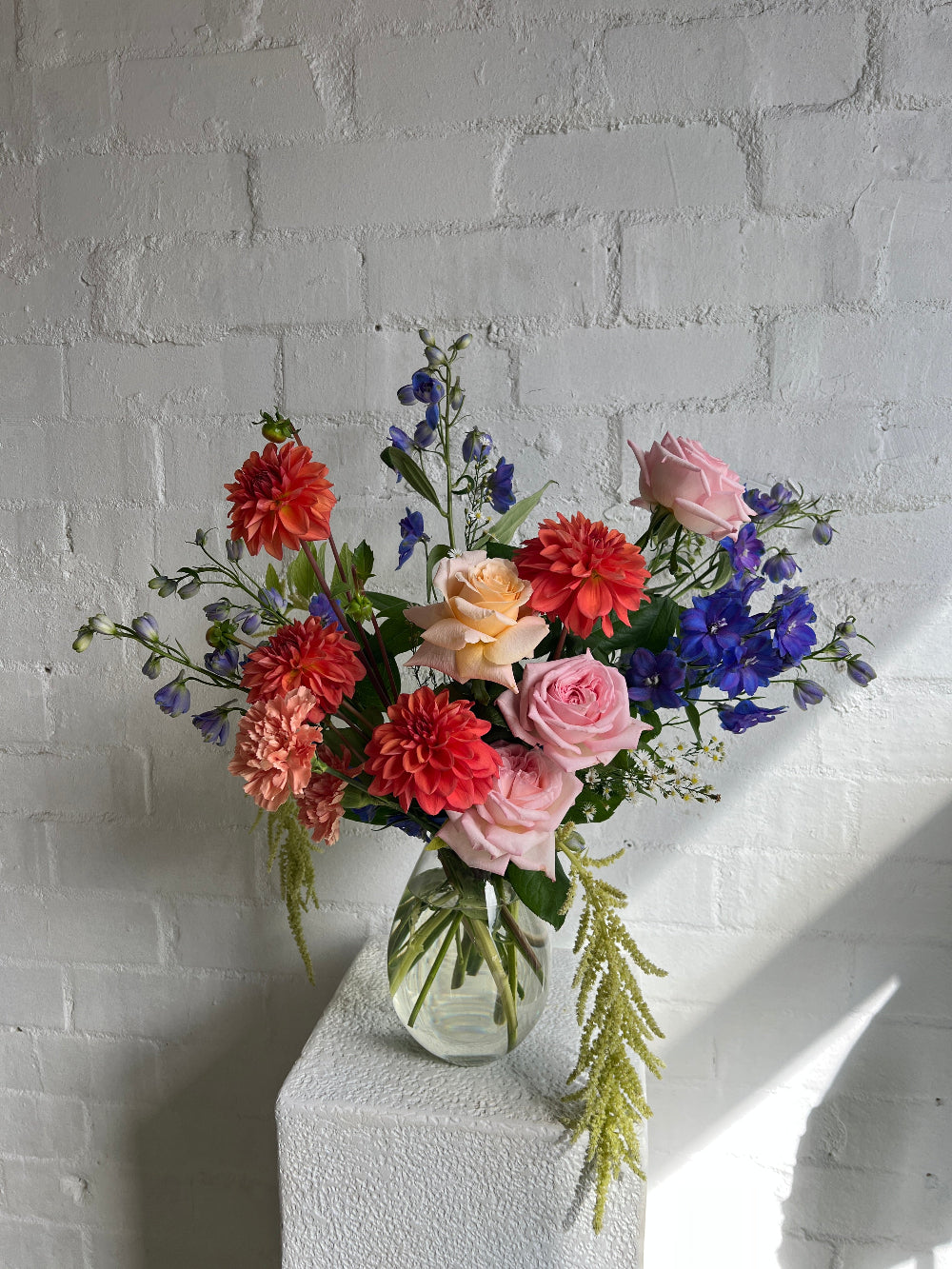 A bright vase of flowers including dahlias, roses,delphiniums and amaranthus.