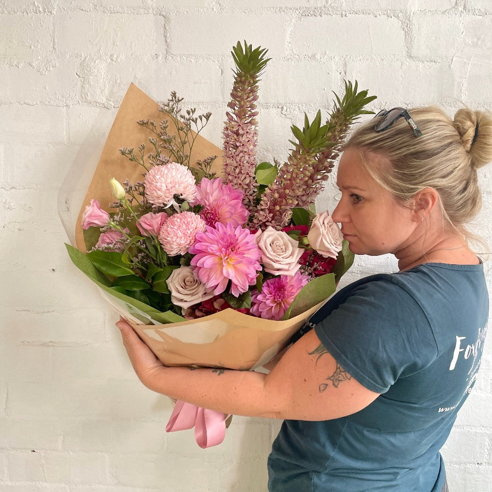 Florist holding a mixed bouquet of pink roses, hydrangea, pink dahlias and pineapple lily gift wrapped in bronze wrapping