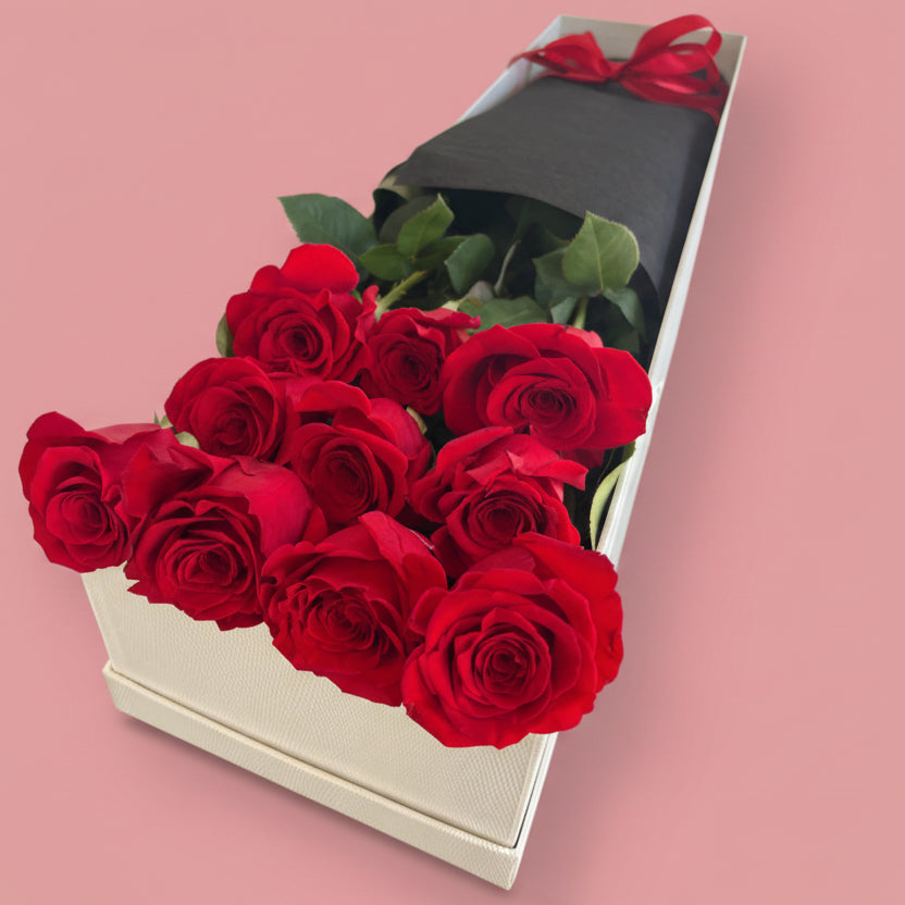 A bunch of premium bright red roses wrapped in black paper in a long white gift box.