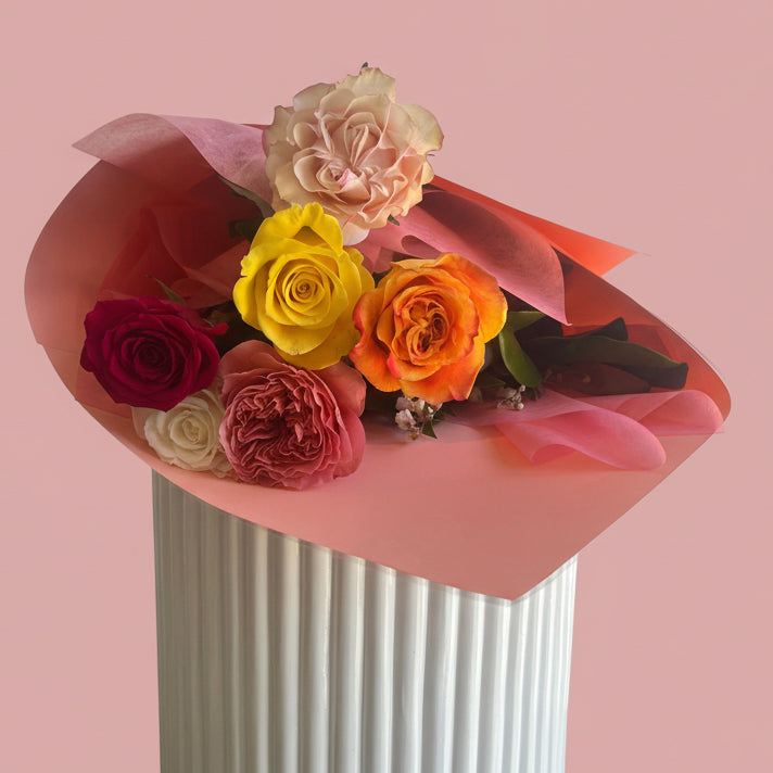 premium mixed colour rose bouquet gift wrapped and presented on top of a white plinth