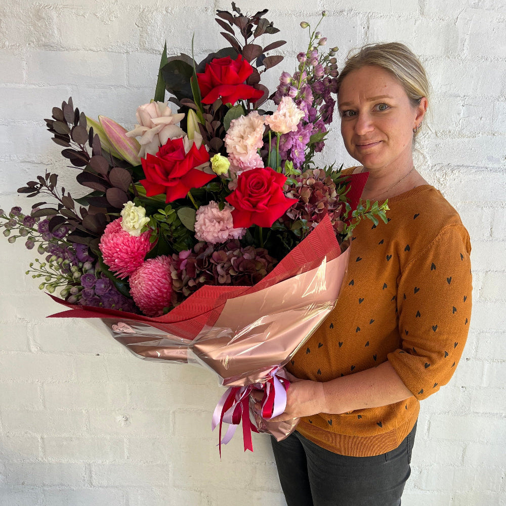 A florist holding a big bouquet of fresh valentines day flowers, gift wrapped and ready to deliver.