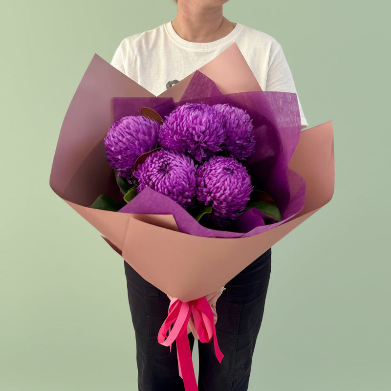 Florist holding a bunch of purple disbuds wrapped in premium wrapping with a pink bow