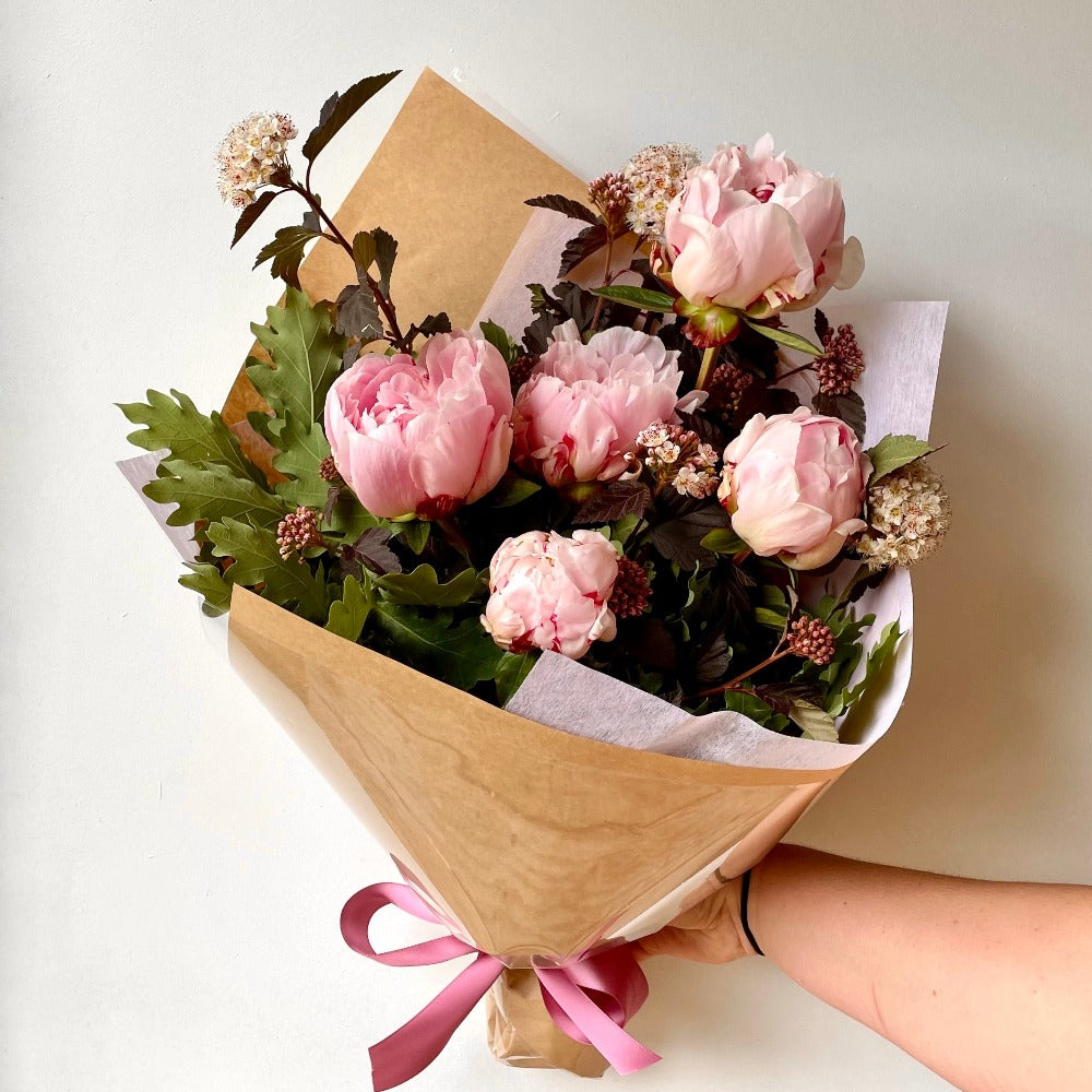 pink Peonies flowers with foliage wrapped in craft paper and tied with a pink bow